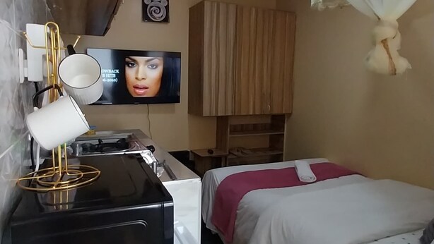 A hotel room with a bed, a desk with a computer, a TV, and a ceiling light. - Tranquil studio apartment in welcoming Thika neighborhood. (Thika)