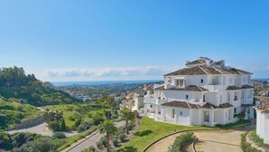 A multi-story white building with a tiled roof, surrounded by greenery and a curved road. - Elegant Penthouse Duplex, Sea and Mountain View close to Puerto Banús (Marbella)