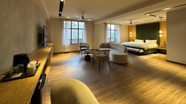 A modern hotel room with a large bed, a seating area with chairs, a small table, and a TV. - IFQ Premier Skardu (Skardu)