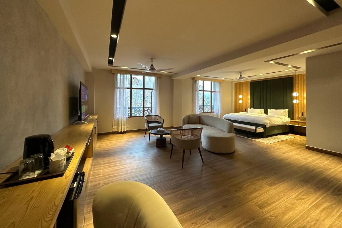 Una habitación de hotel moderna con una cama grande, un área de descanso con sillas, una mesita y un televisor.