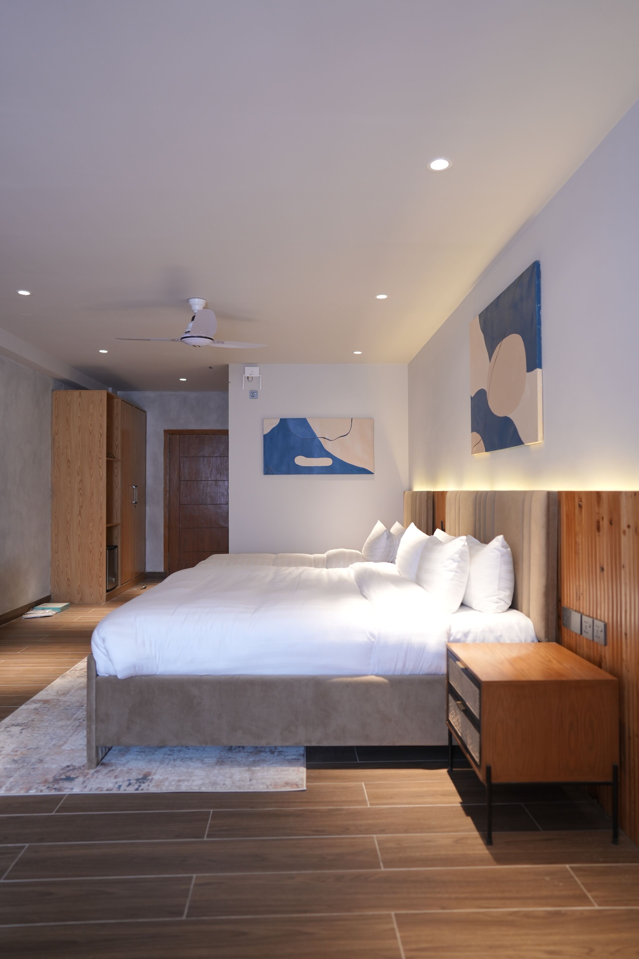 A modern bedroom with a large bed, wooden wardrobe, and abstract wall art.