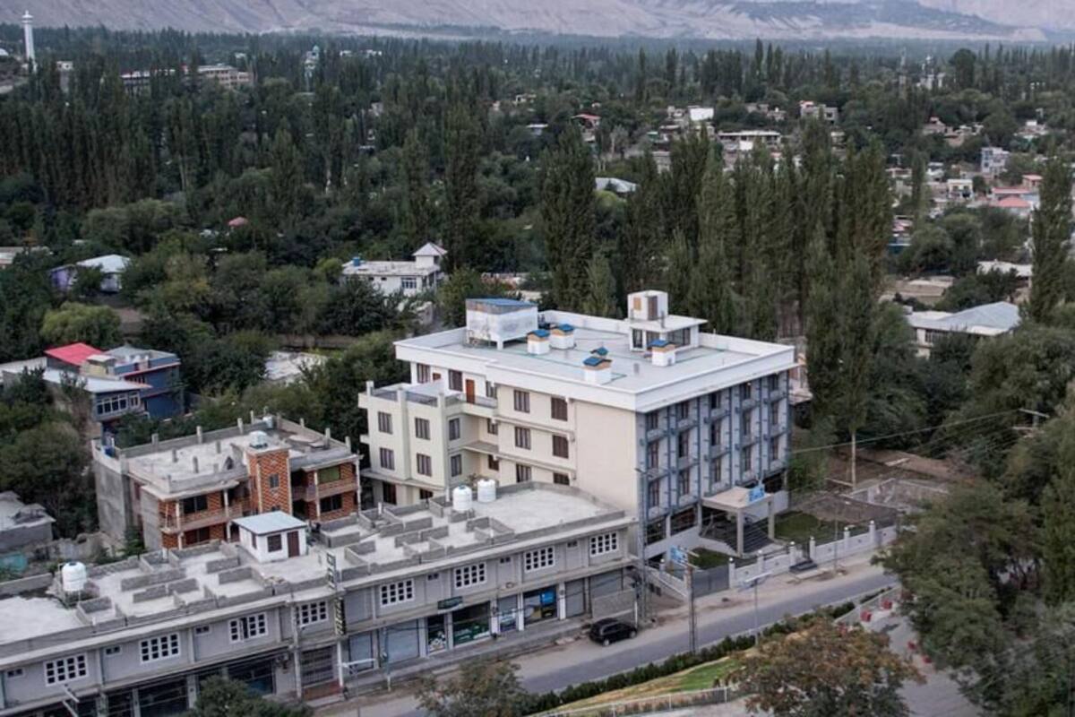 Un edificio de varios pisos con techo plano, rodeado de árboles frondosos y otros edificios.