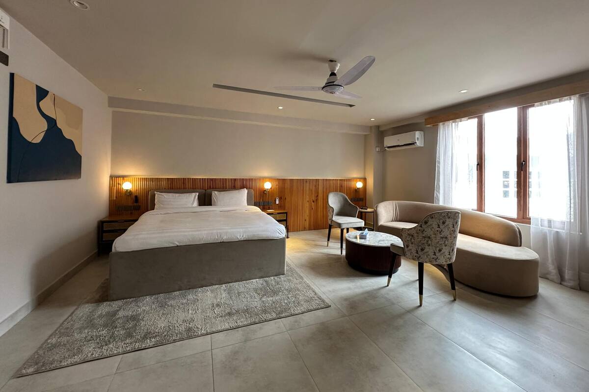 Una habitación de hotel moderna con cama, escritorio, silla, sofá, ventilador de techo y una ventana grande.