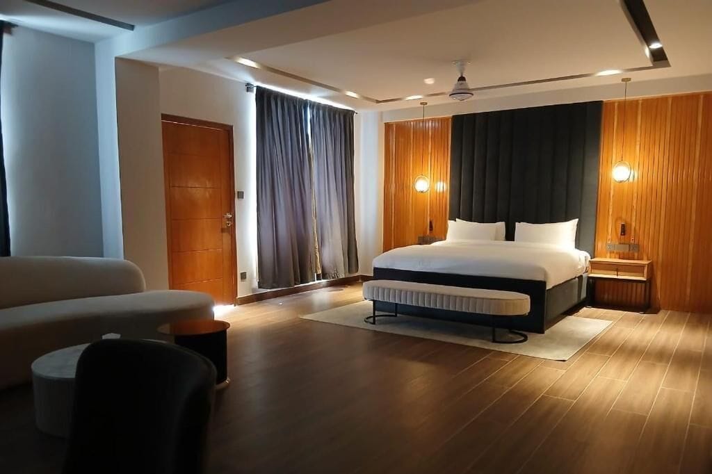 A modern hotel room with a large bed, a sofa, a wooden floor, and a ceiling fan.