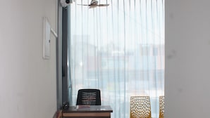 Una habitación con ventilador de techo, un escritorio, dos sillas y una ventana con cortinas traslúcidas.