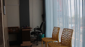 Una habitación con un escritorio, dos sillas, un bote de basura y una cortina.