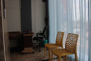 Una habitació amb una taula de treball, dues cadires, un safataire i una cortina.