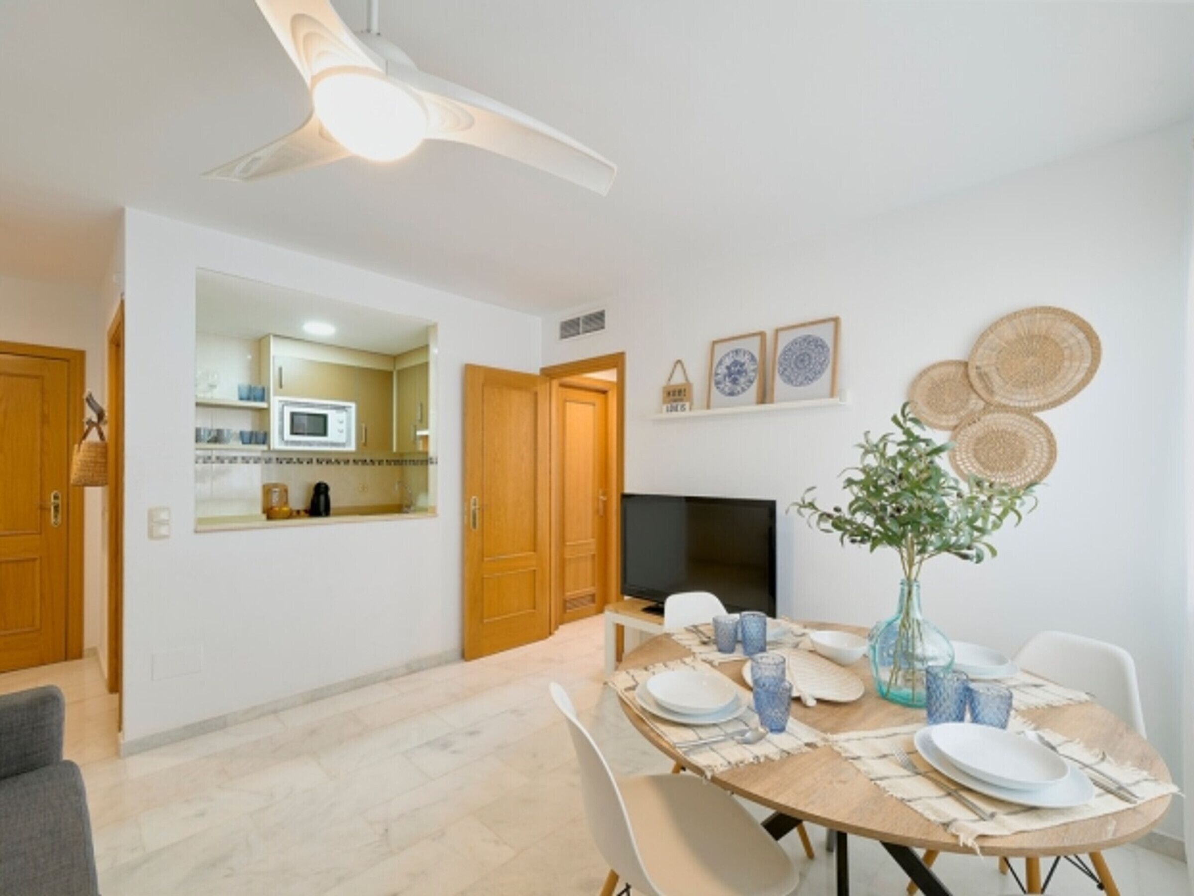 A dining area with a table set for four, a television, and a kitchen visible through an open door.