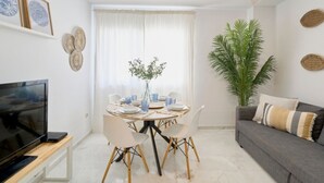 Ein modernes Wohnzimmer mit Flachbildfernseher, Esstisch mit Stühlen, Deckenventilator und einer großen Pflanze.