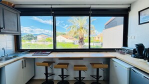 Een moderne keuken met een groot raam, barstoelen en een koffieapparaat.