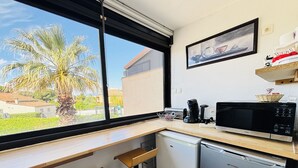 Een compacte keuken met uitzicht op palmbomen, inclusief een magnetron, koffiezetapparaat en vaatwasser.
