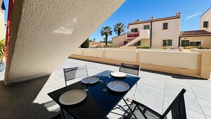 Een terras met tafel en stoelen, een zwembad en een gebouw met een rood dak op de achtergrond.