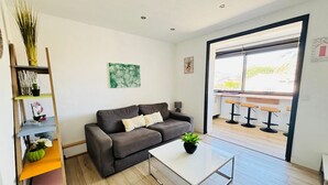 Een moderne woonkamer met een grijze bank, een salontafel, een boekenkast en een groot raam.