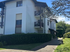 Ein zweistöckiges Gebäude mit Balkon, Kiesweg und Hecke.
