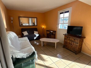 A living room with a sofa, a television on a wooden cabinet, a small table, and a window with a view. - Apartment with air conditioning, port view - 4 guests (Port-Vendres)