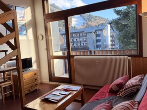 A room with a large window, a wooden desk, a bed with pillows, a radiator, and a TV on a wooden stand. - Central apartment, pets welcome - 6 guests, south balcony (Arâches-la-Frasse)