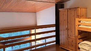 Ein Zimmer mit schräg versiegelter Decke, Holzbettställen, einem Kleiderschrank und einem Fenster mit Blick.