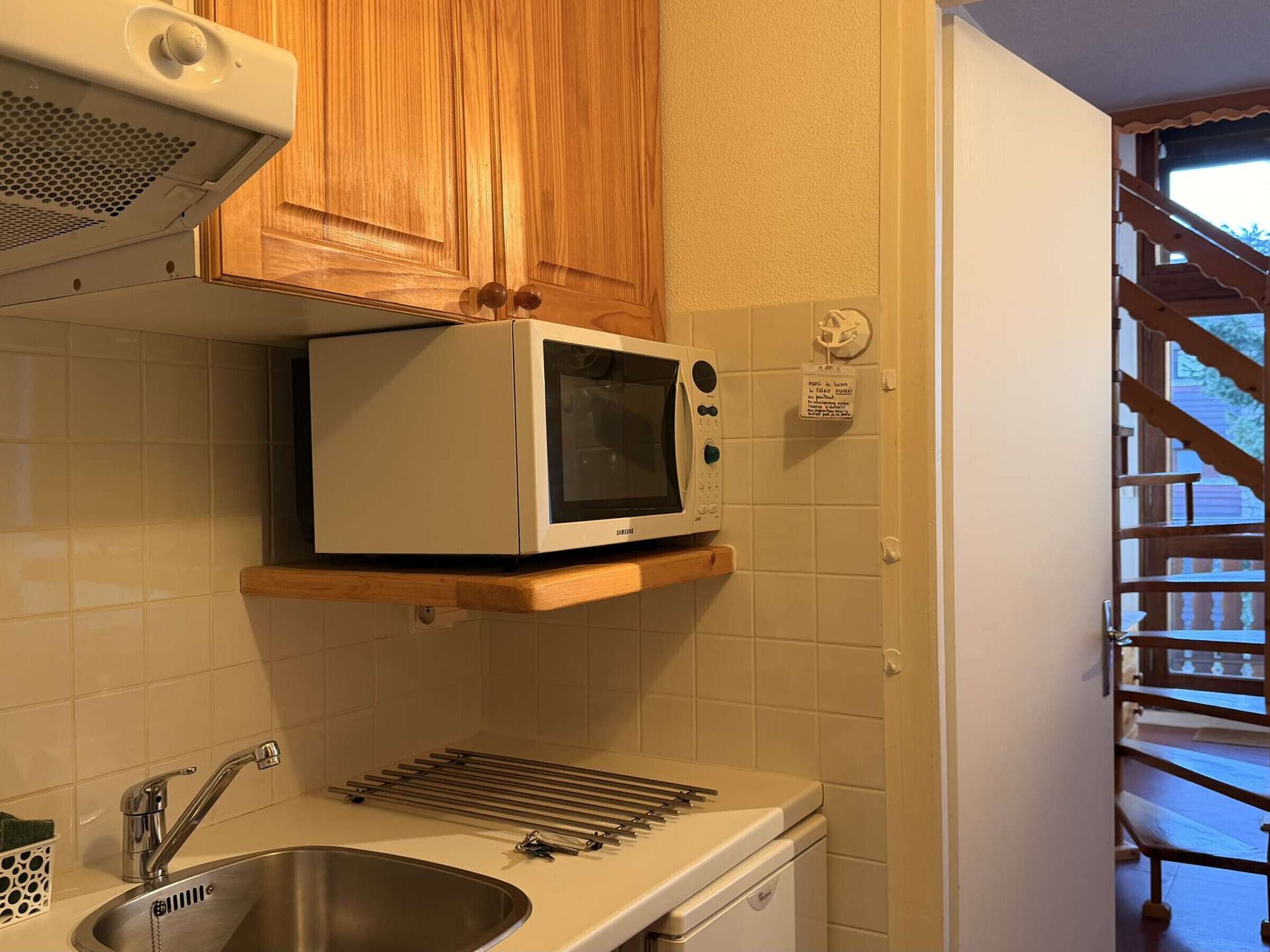A kitchen with a microwave, a sink, and wooden cabinets.