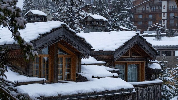 Une cabane en bois traditionnelle, avec un toit enneigé, de grandes fenêtres et des fondations en pierre.