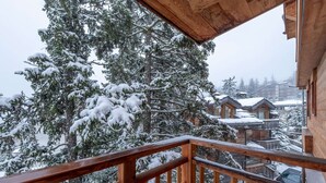 Un balcon en bois offrant une vue sur des arbres et des bâtiments recouverts de neige.
