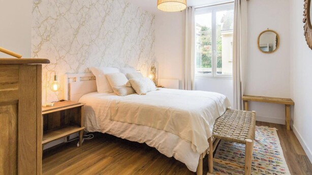 Ein Schlafzimmer mit Bett, Nachttisch, Lampe und Blick ins Freie.