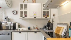 Eine Küche mit weißen Schränken, einer Kaffeemaschine, einer Mikrowelle, einem Spülbecken und einer Wanduhr.