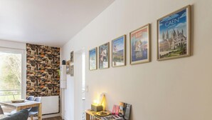 Ein Zimmer mit Stehwand, einem Esstisch mit Stühlen, einer Lampe und gerahmten Postern an der Wand.