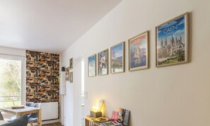 Ein Zimmer mit Stehwand, einem Esstisch mit Stühlen, einer Lampe und gerahmten Postern an der Wand.