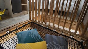 A room with a wooden crib, a small play area with a toy, and a hammock.