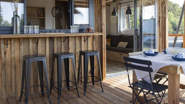A wooden deck with a bar area, stools, and a table with chairs.
