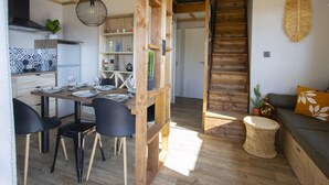 A modern kitchen with wooden beams, a dining area with black chairs, a staircase, and a living area with a sofa and a cactus plant.