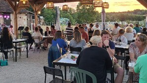 Een terras met tafels en stoelen, overdekt door een houten constructie met hangende lampen.