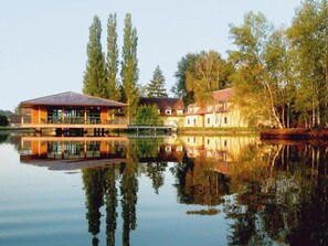 Una propiedad junto al lago con una construcción grande, una estructura más pequeña y altos árboles.