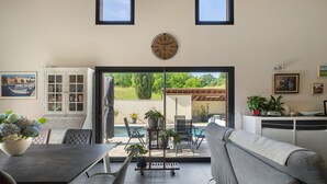 Ein modernes Wohnzimmer mit Essbereich, einer Couch, einem Couchtisch und Blick auf einen Pool und Grünflächen.