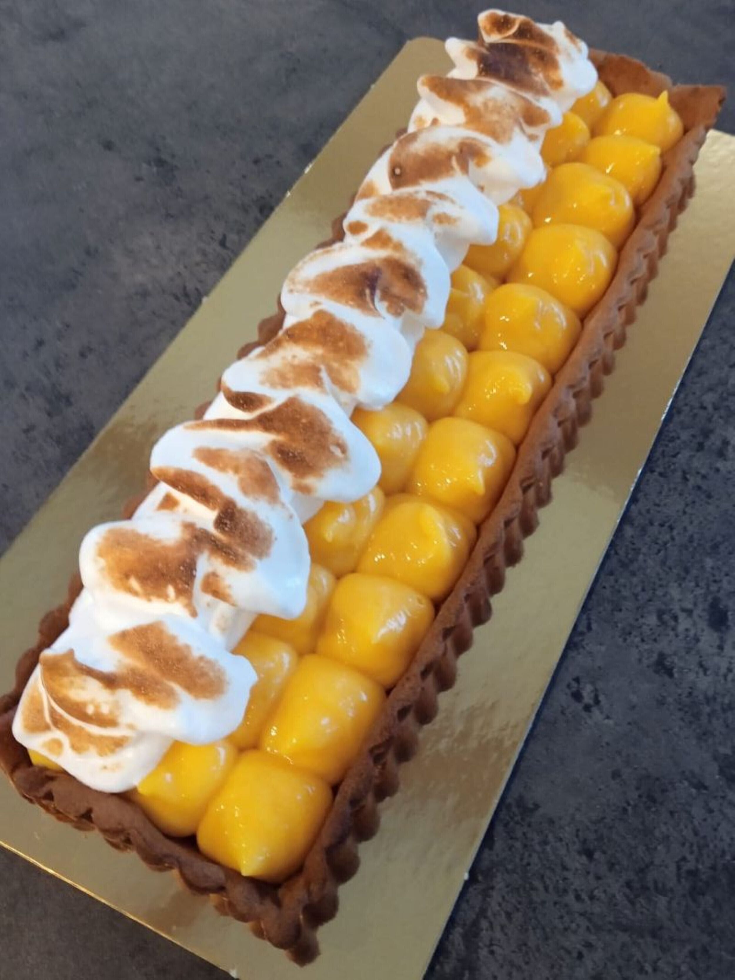 Een dessert met een romige topping en geel fruit in een taartbodem.