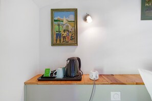 Una stanza con un tavolo di legno, un bollitore, un telefono, un quadro incorniciato e una lampada a parete.