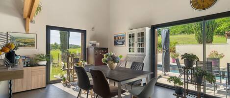 A modern kitchen with a dining table, chairs, and a large window overlooking a garden.