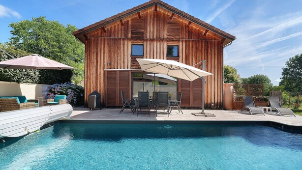 Ein Holzgebäude mit Pool, Gartenmöbeln und einer Pergola.