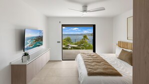 Quarto com cama, TV, ventoinha no teto e vista para o exterior.