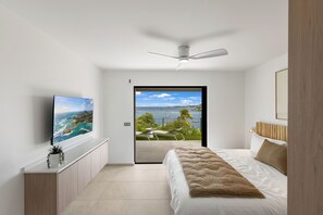 A bedroom with a bed, a TV, a ceiling fan, and a view of the outdoors. - Villa Élios, intimate and elegant. Exceptional sea view facing Saint-Barthélémy. (Saint Martin)