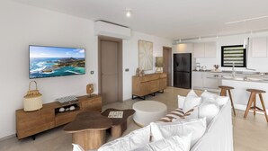Uma sala de estar moderna com televisão de tela plana, um sofá, uma mesa de centro e uma área de jantar com banquetas.