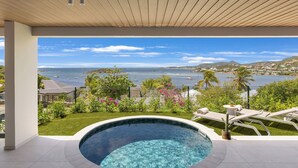 Piscina com vista para o oceano e colinas, rodeada por vegetação e uma área cercada.