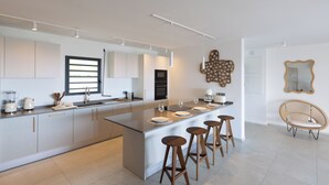 Cozinha moderna com ilha central, banquetas e área de jantar com uma cadeira.