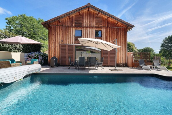 A wooden building with a pool, outdoor furniture, and a pergola.