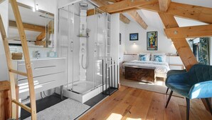 A modern bedroom with a wooden ceiling, a glass shower, a bed with blue bedding, and a blue chair. - Guest Room "Le Séchoir de Saint Vincent - Brame" near Sarlat – Pool, Wi-Fi, Air Conditioning (Saint-Vincent-le-Paluel)