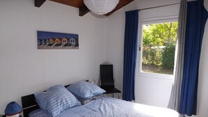 Et soveværelse med en seng, et natbord, en lampe, et billede og et vindue med gardiner.