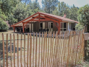 Une cabane en bois dotée d’un patio couvert, entourée d’une clôture en bois et d’une clôture de barbelés.