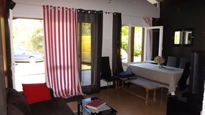 En stue med sofa, sofabord, spisebord med stole og et fjernsyn. Et vindue med gardiner og en dør, der fører ud.
