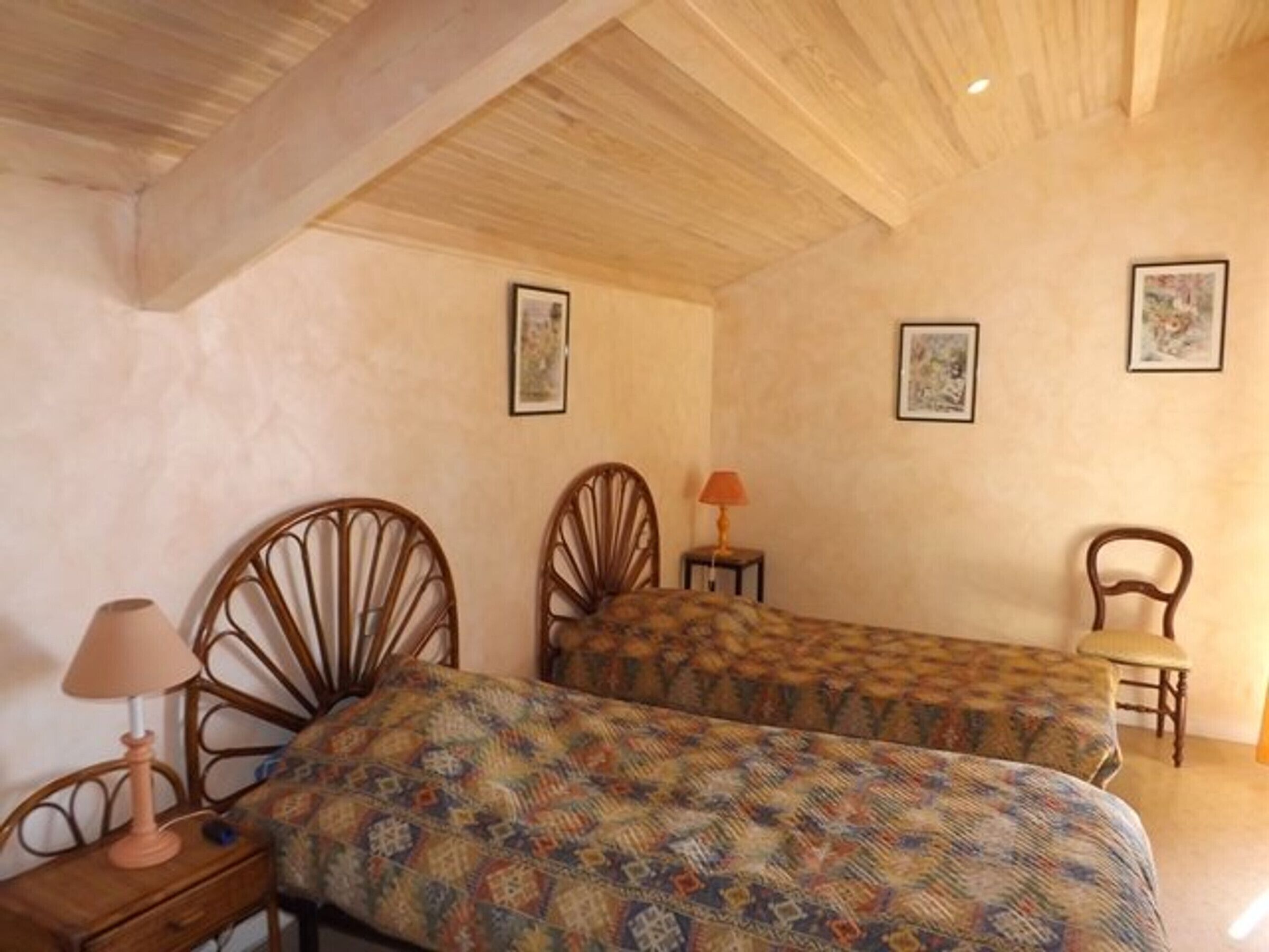 A bedroom with two wooden beds, a nightstand, a chair, and a lamp.