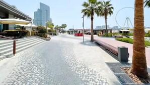 A paved walkway with palm trees, a Ferris wheel, and modern buildings in the background. - Premium 3BR plus maid room -Beachfront -Monthly Stay (Dubai)